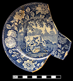Pearlware saucer underglaze printed in medium blue in Milkmaid pattern.  Continuous repeating floral border.   One of two matching vessels from this assemblage.  This piece is unmarked, but identical pattern and border have been found with the mark of Thomas Rathbone & Co., 1810 – 1845, Portobello, Scotland.  5.00” rim diameter, 1.00” vessel height.